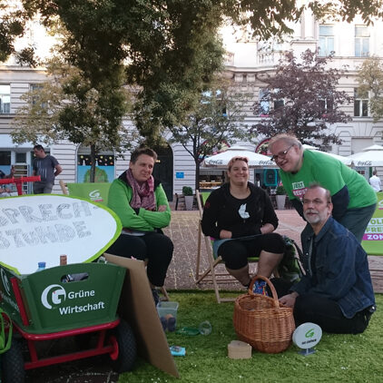 Vier Personen sitzen im Freien unter einem Baum auf einem grünen Teppich