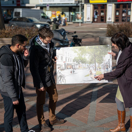 Barbara Pickl und Aktivisten unterhalten sich am Gaußplatz stehend über ein Mockup der geplanten Wallensteinstraßenumgestaltung